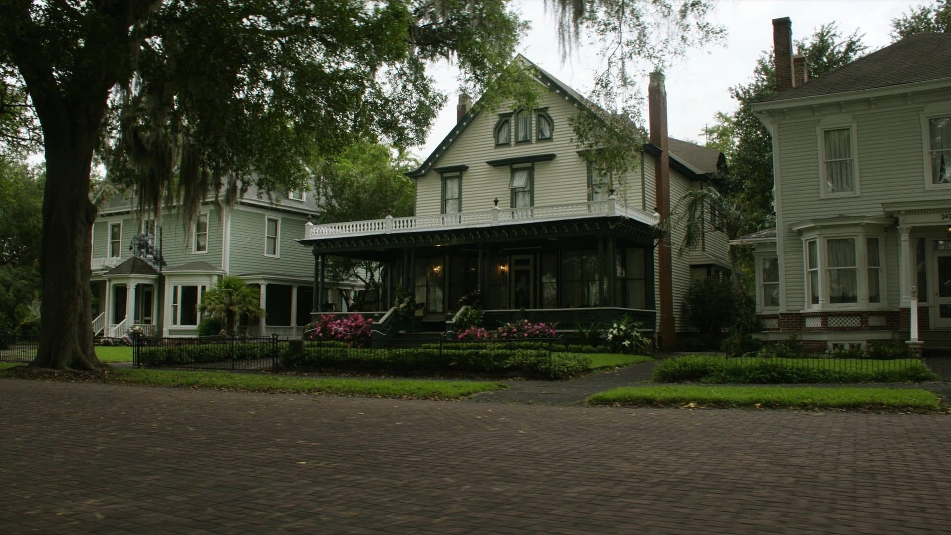 Early 1900s Victorian and Craftsman homes with wraparound porches on a brick paved street in DeLand, Florida, shaded by live oaks with Spanish moss.