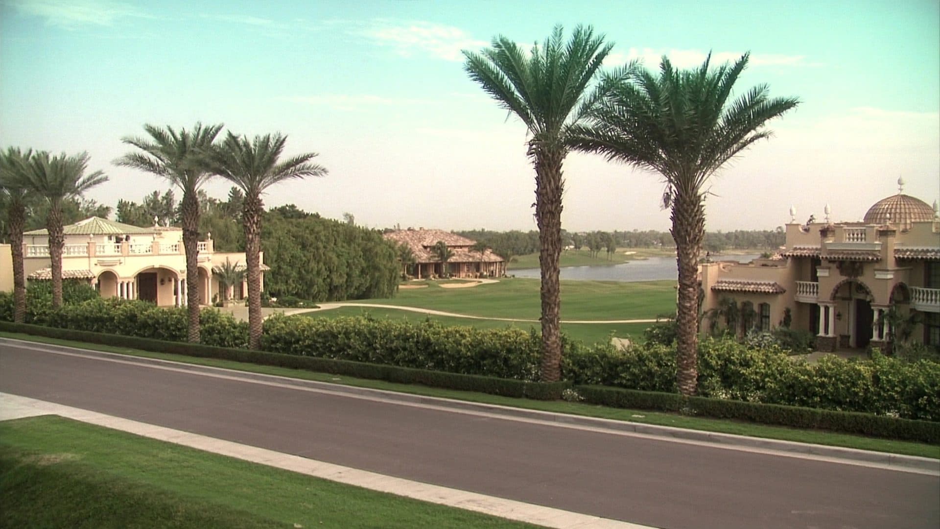 Landscaped boulevard in Heathrow, Florida lined with royal palms, leading past large Mediterranean revival stucco homes with barrel tile roofs.