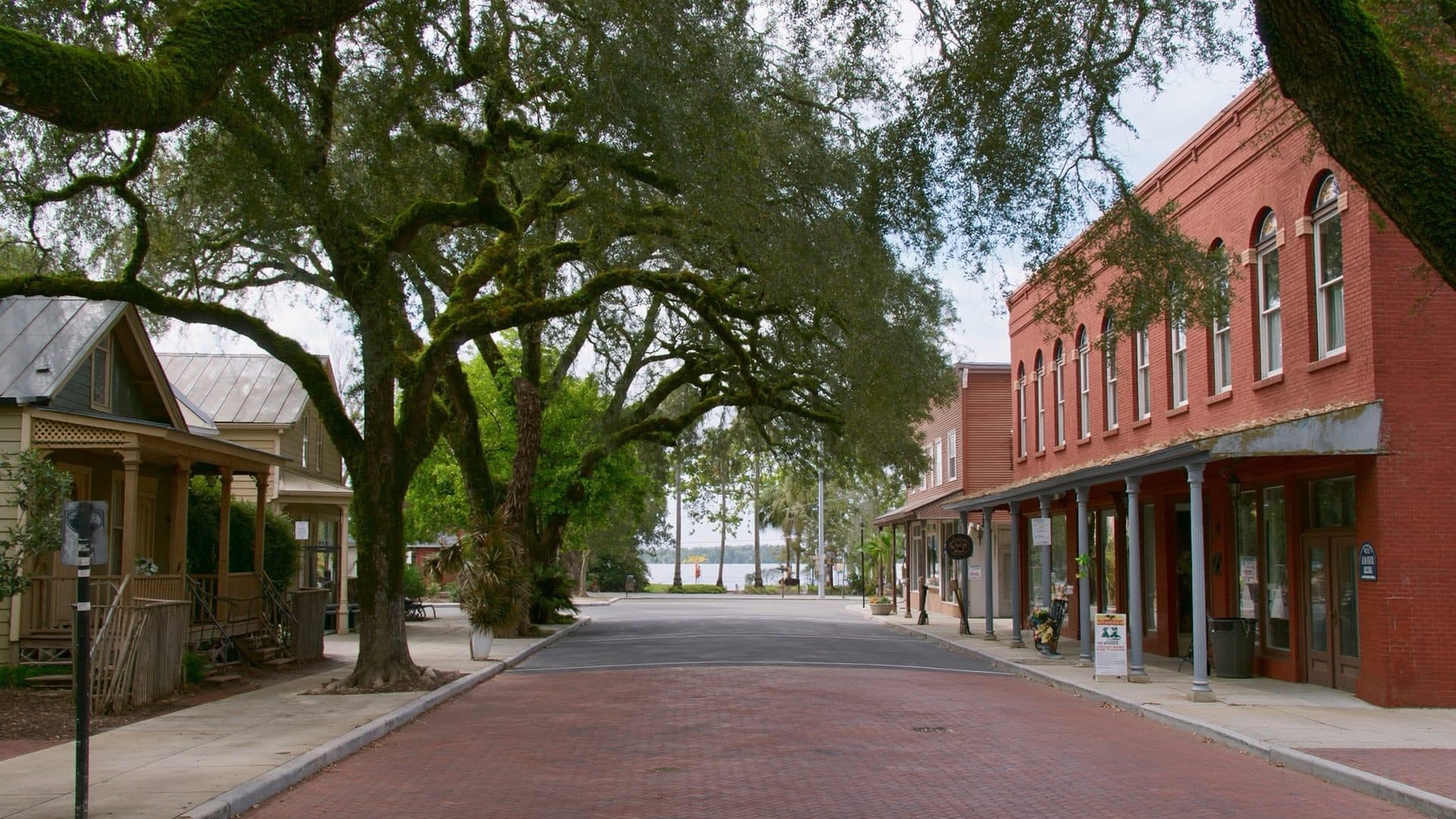 Brick paved street in the historic district of Sanford, Florida, with a red brick storefront building, live oaks overhead, and Lake Monroe visible at the end of the street.