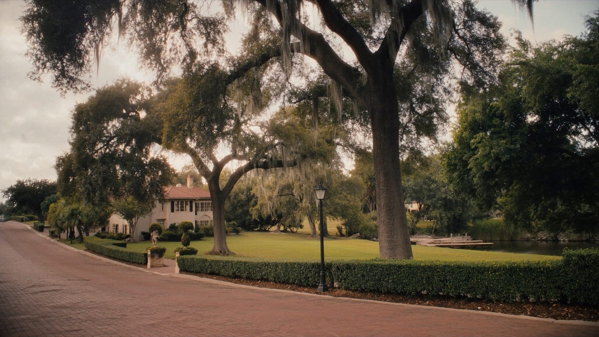 Brick paved residential street in Winter Park, Florida beneath immense live oaks, with Mediterranean revival homes and one of the chain of lakes beyond.