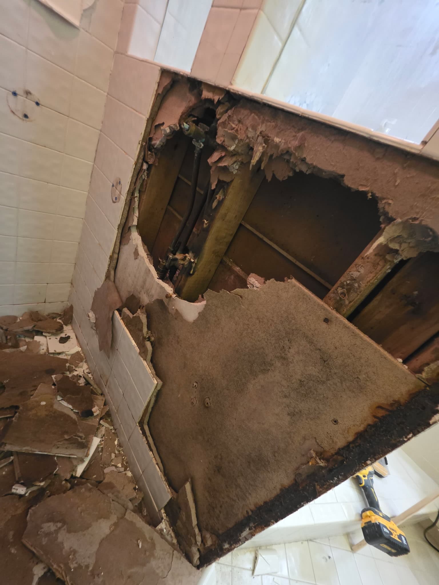 A bathroom ceiling cut open and hanging away, its back face darkened by water, with the joists above exposed