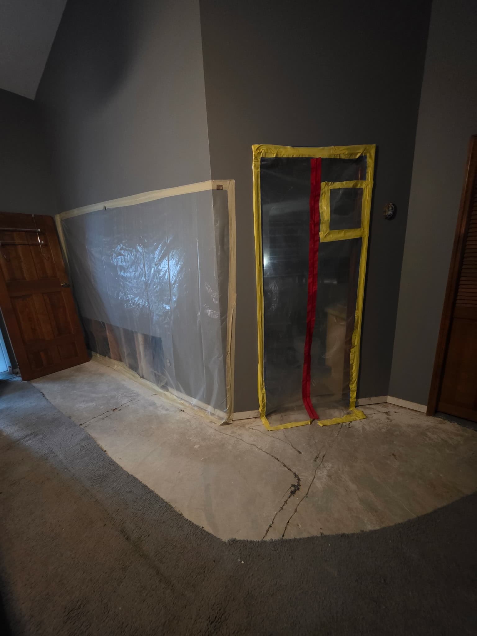 A sealed containment barrier built across a bedroom, with plastic sheeting taped to the walls and a zippered entry door framed in yellow tape