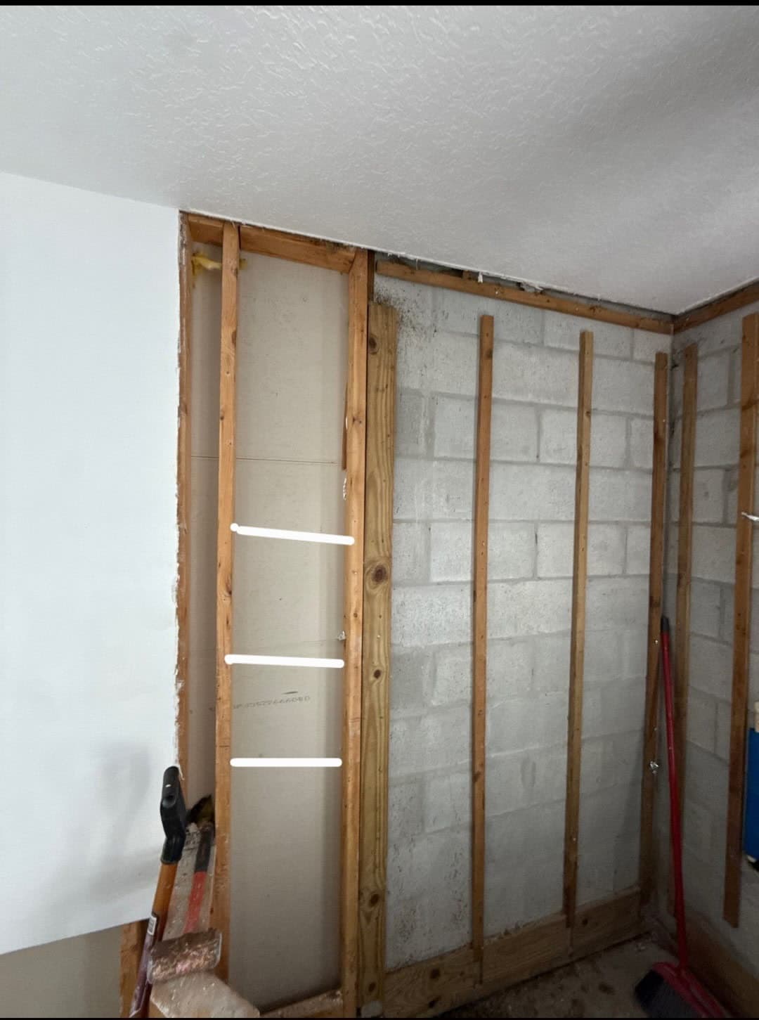Drywall removed from a concrete block wall, exposing furring strips and mold staining along the top plate