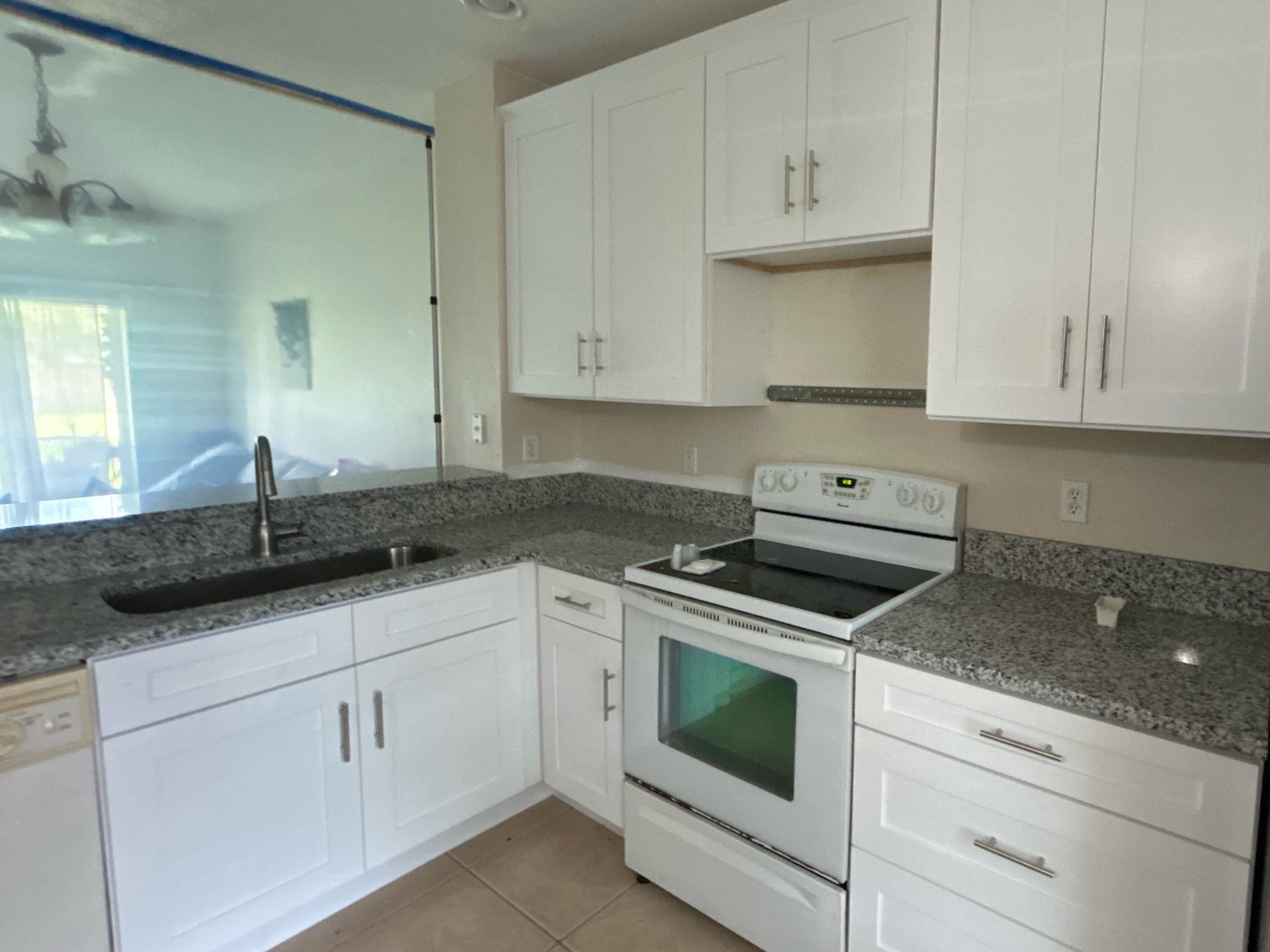 A kitchen rebuilt after restoration, with new white shaker cabinets, speckled granite counters, a new range and an undermount sink